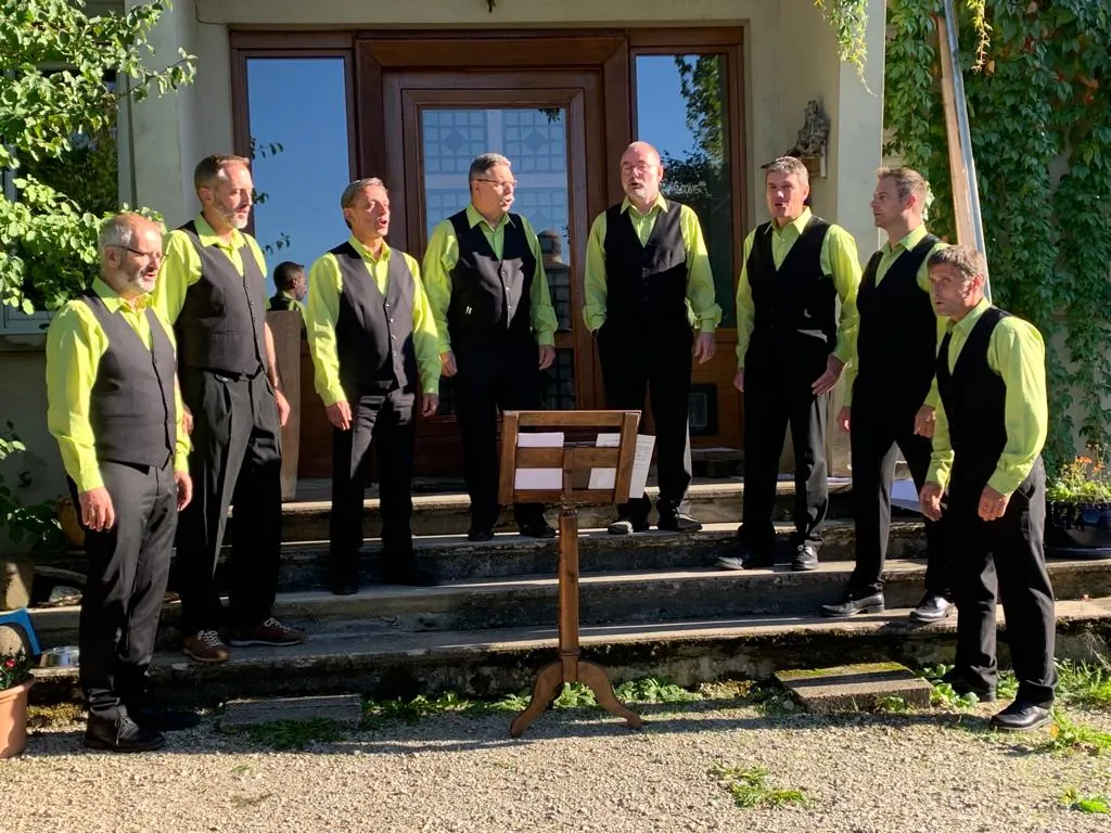 Les huit chanteurs en plein air, devant une maison, un pupitre au premier plan